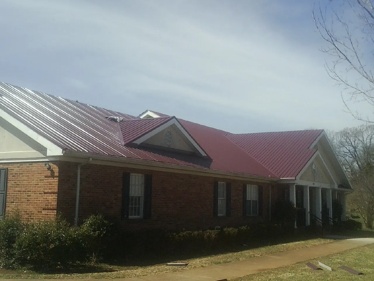 Red metal roof with gabled entries on a long brick building, from a Hail Damage Roof Repair job in Edmonton