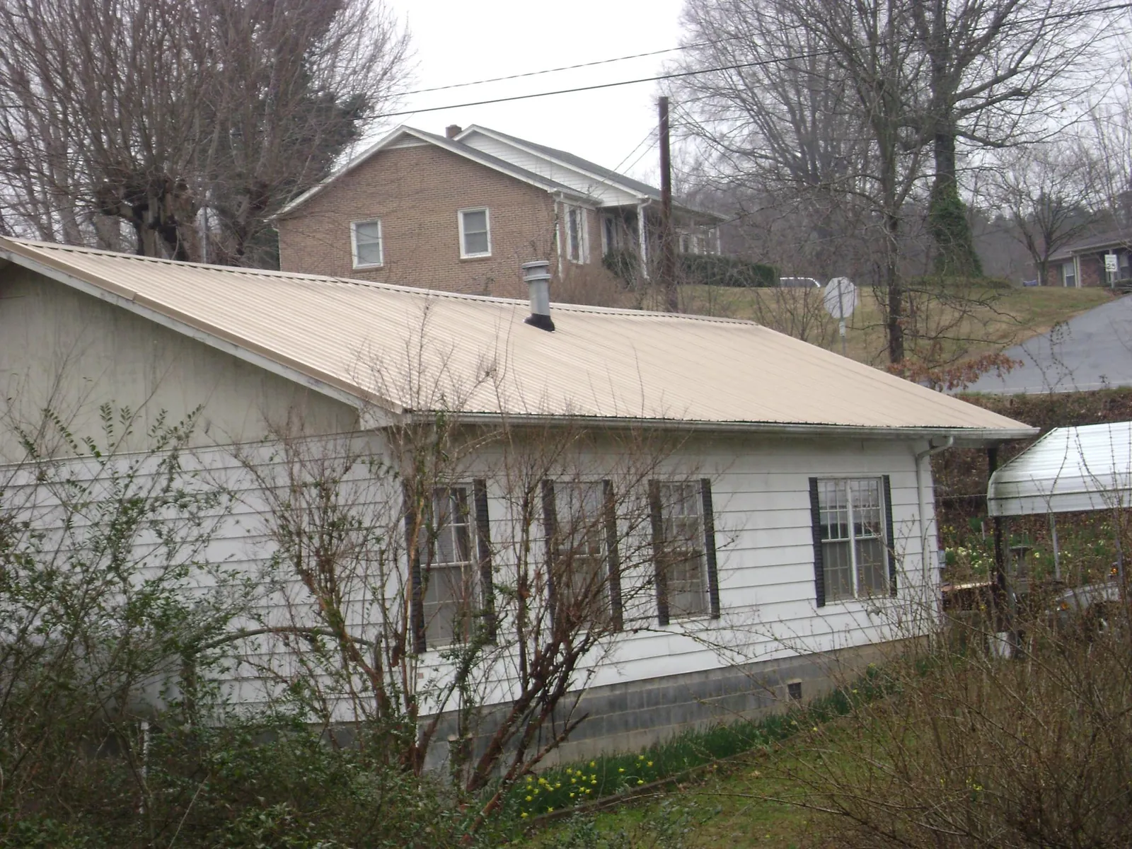 Tan metal roof on a white sided house set into a hillside — Commercial Roofing by Roofing Brothers in Edmonton